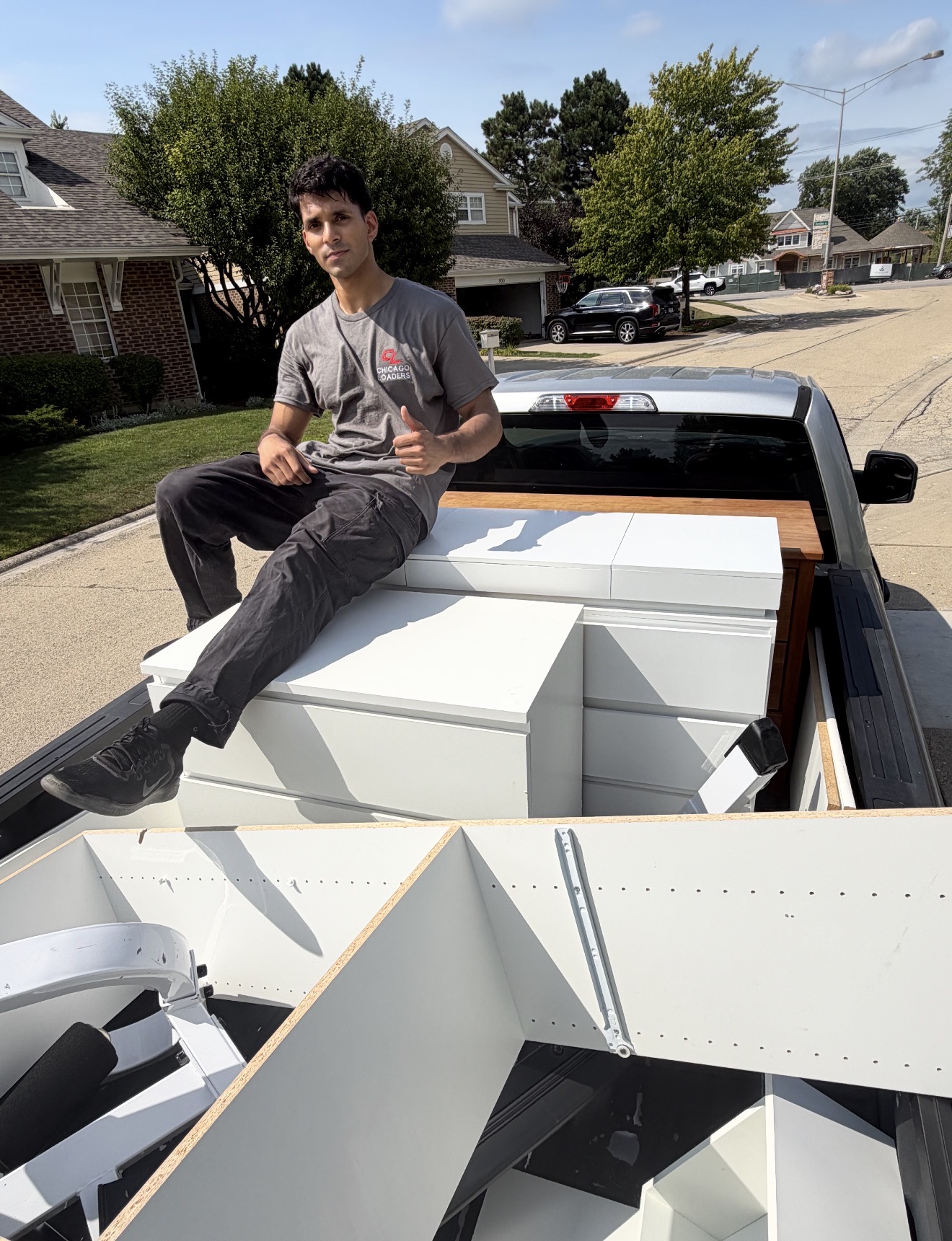 Mover sitting on white furniture loaded in a pickup truck bed giving a thumbs up