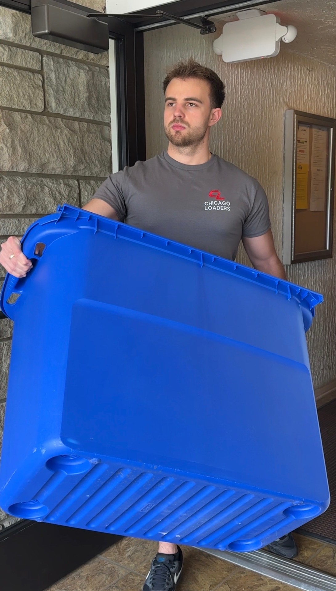 Loader carrying a large storage bin into a building