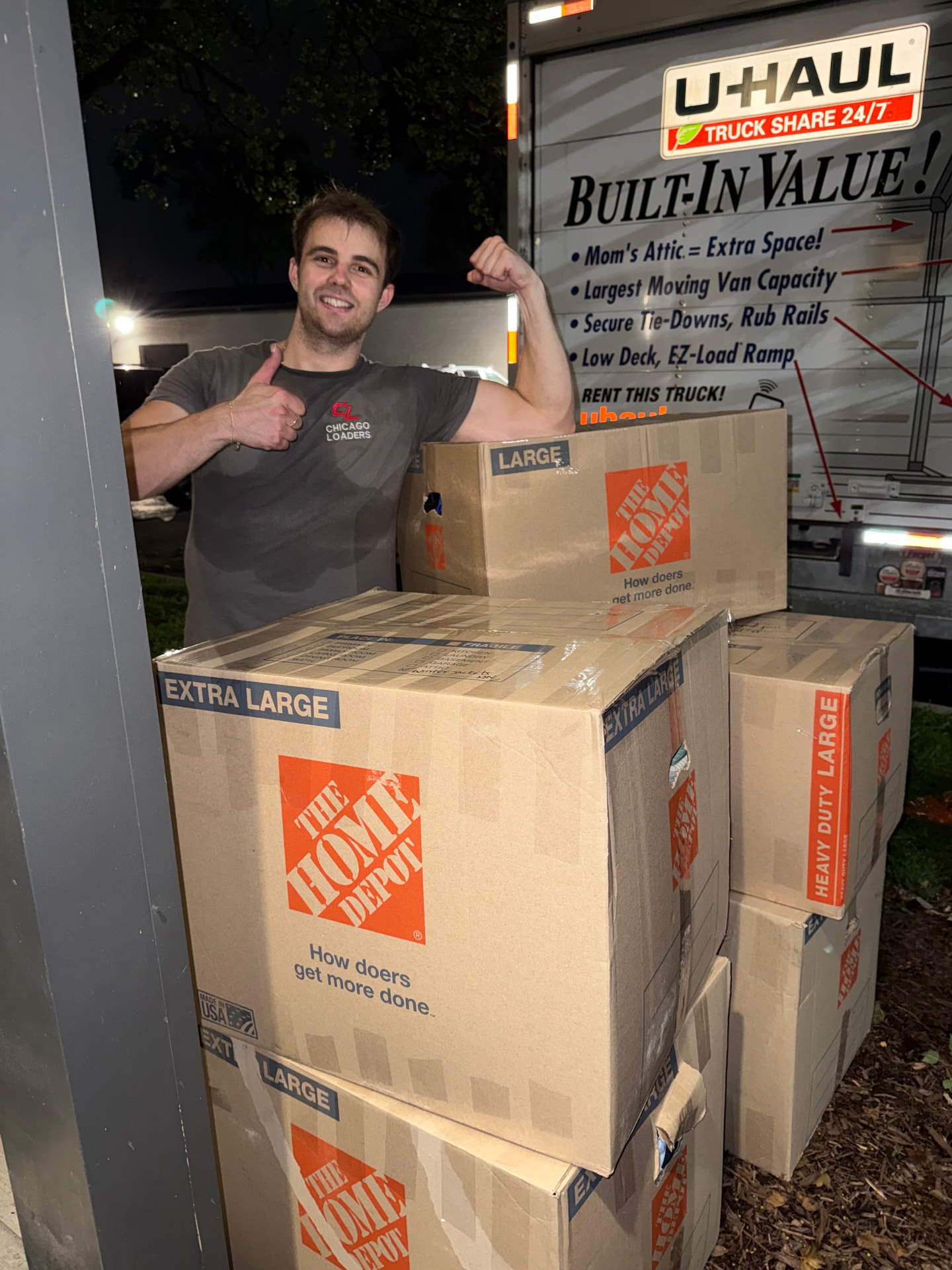 Mover giving a thumbs up next to stacked moving boxes in front of a U-Haul truck at night