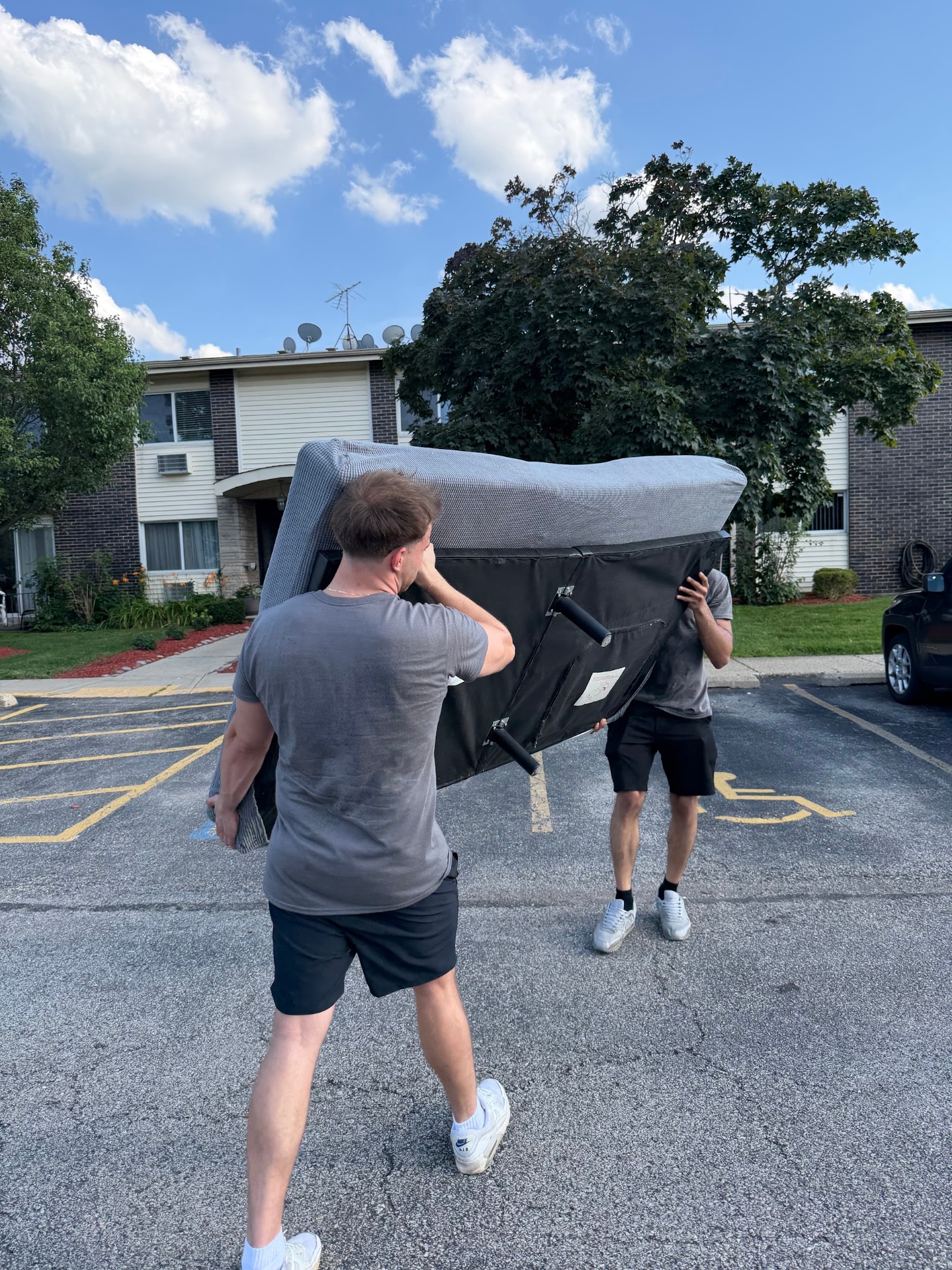 Two loaders carrying a sofa across a parking lot