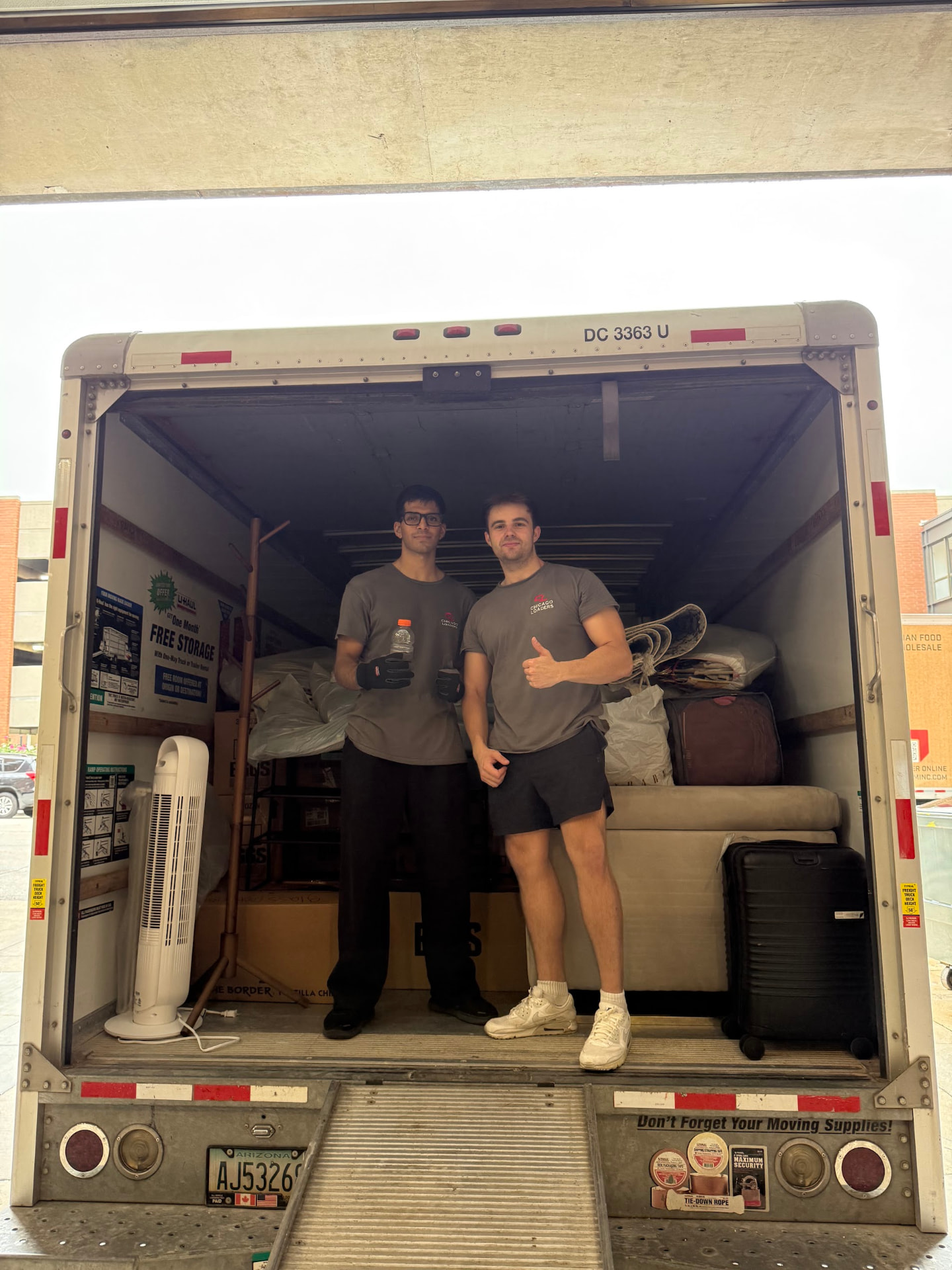 Two movers standing in the back of a loaded moving truck giving a thumbs up