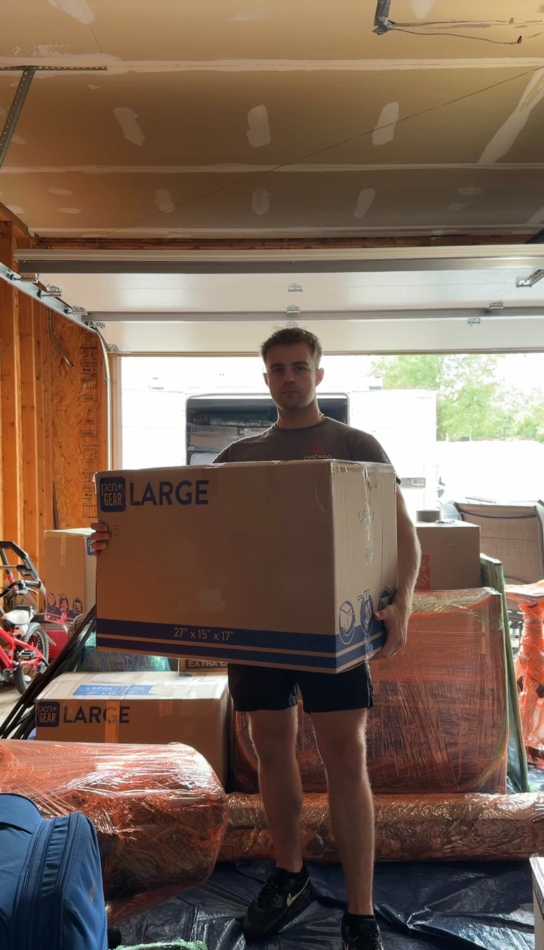 Mover carrying a large moving box inside a packed garage