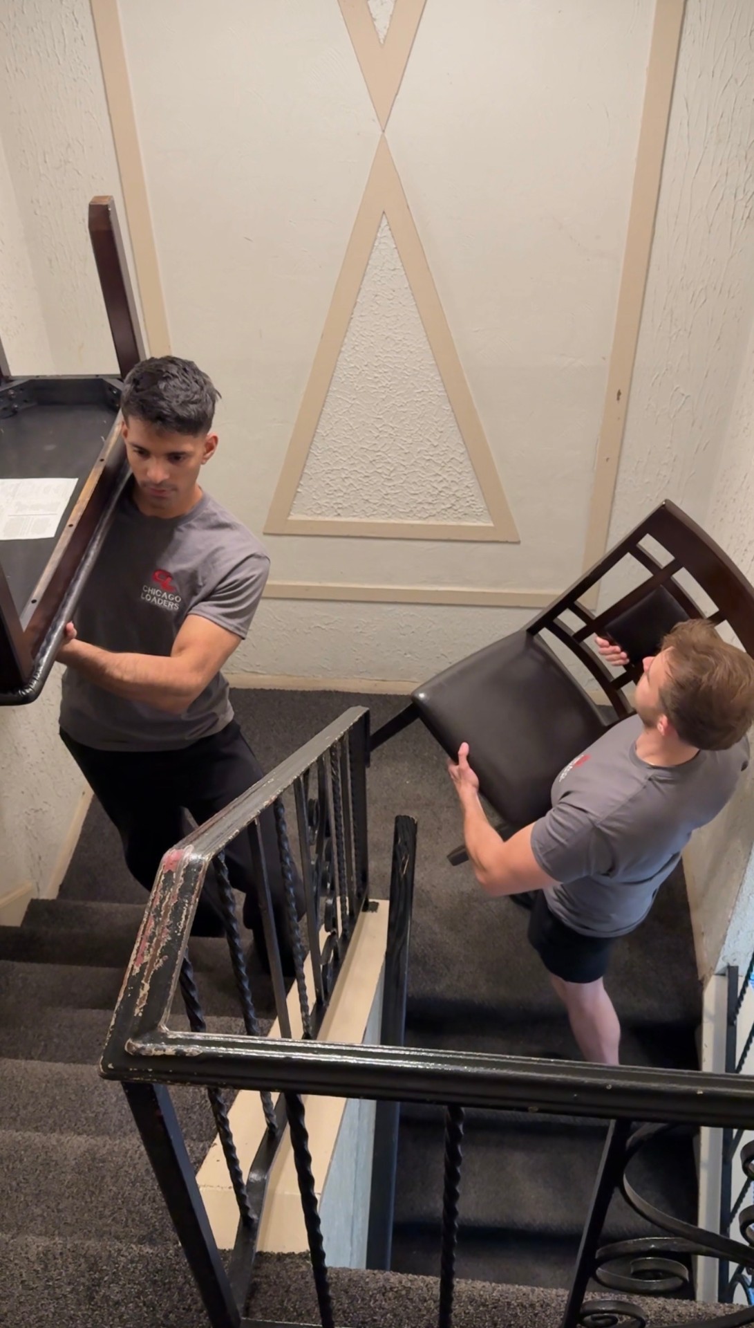 Loaders carrying a chair up a stairwell